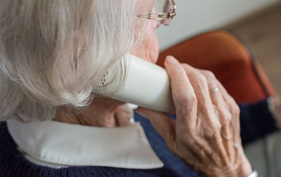 Nachaufnahme einer Senioren von schräg hinten, die ein Festnetz-Telefon an ihr Ohr hält.